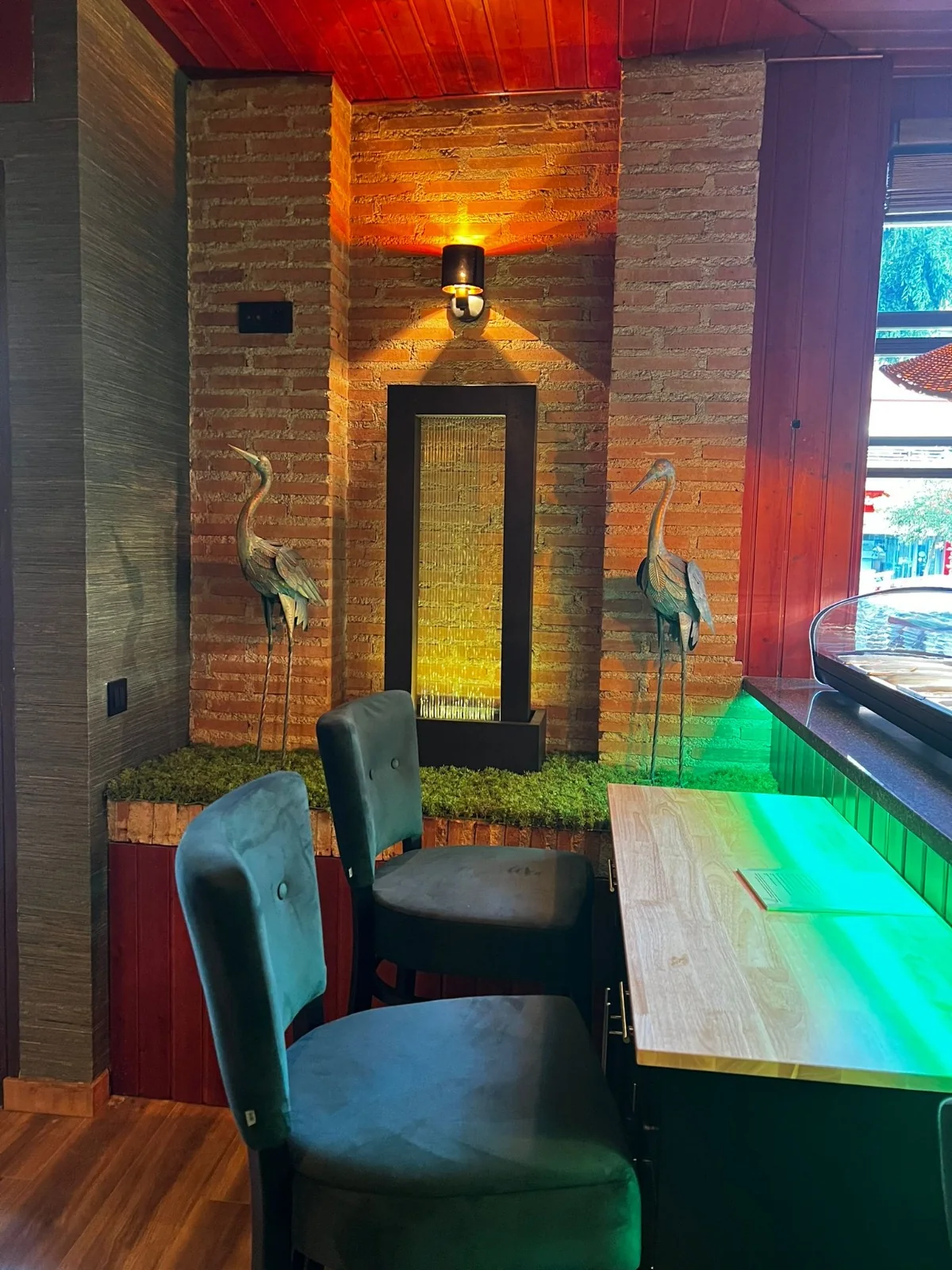 Rincón de Restaurante Manila con pared de ladrillo, esterilla, garzas de bronce y una fuente de agua iluminada